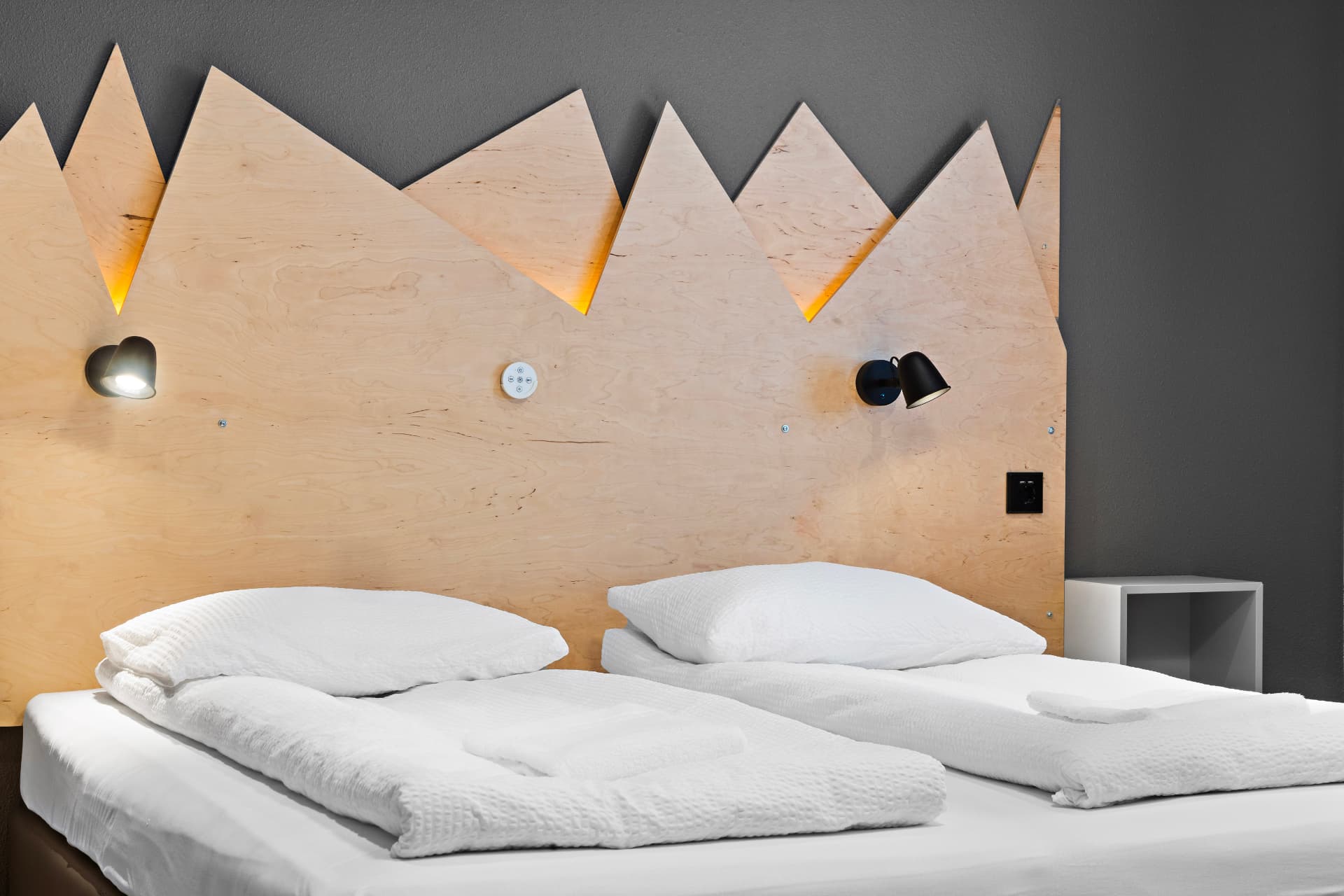 Backlit mountain-shaped wooden headboard above fresh white beds at START Hostel
