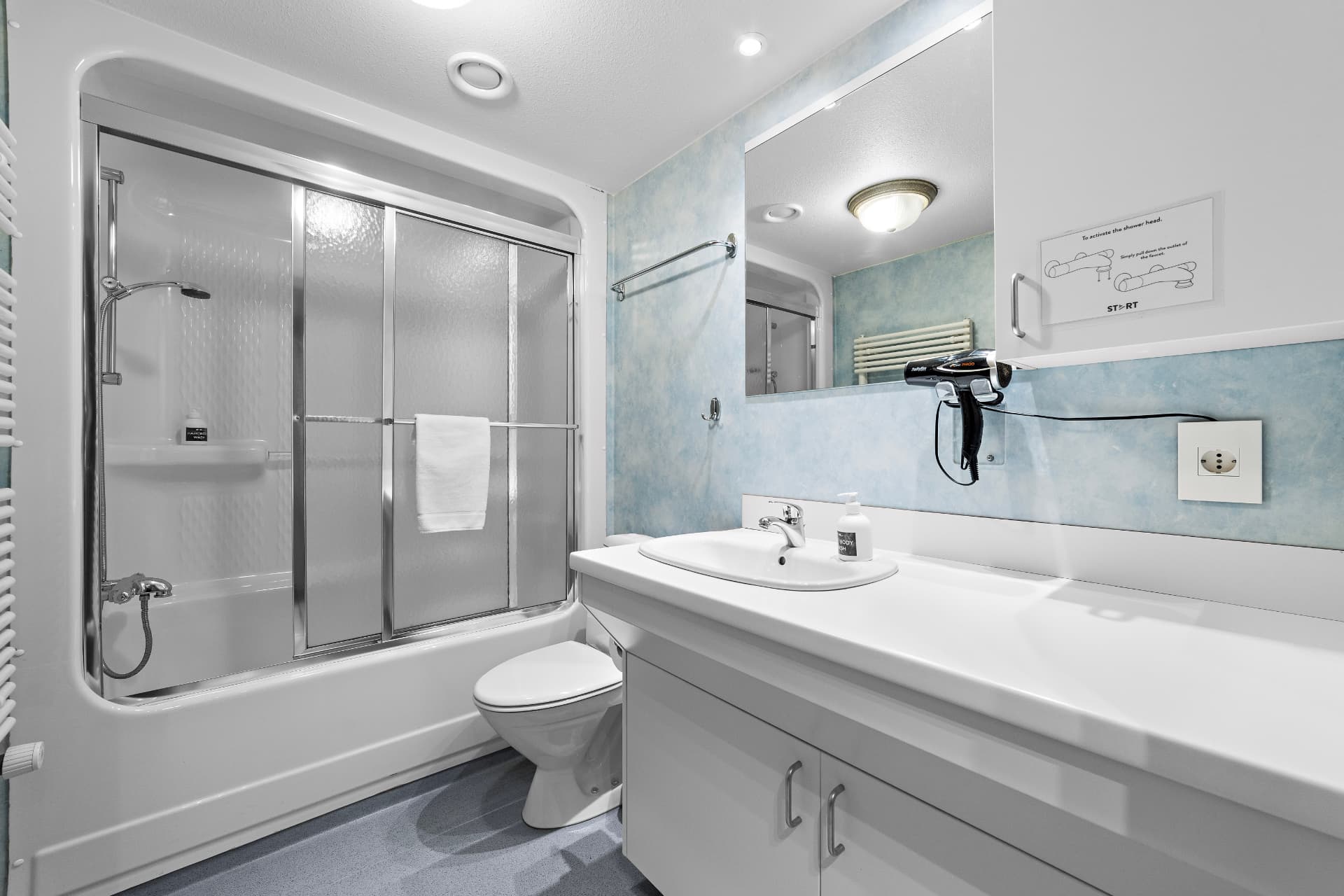 Private bathroom with shower over bath, sink and hairdryer at START Hostel