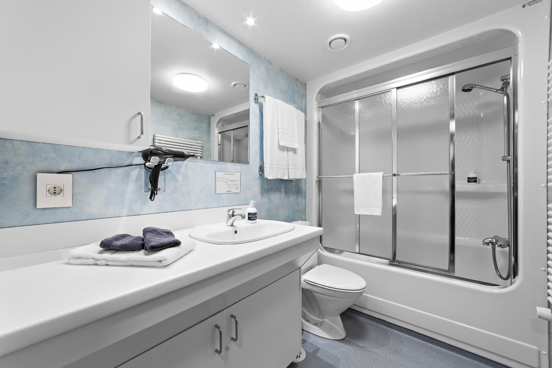 Shared bathroom with sink, mirror, hairdryer and shower over bath at START Hostel